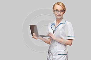 Beautiful Caucasian woman doctor or nurse holding a laptop pc computer standing over grey background