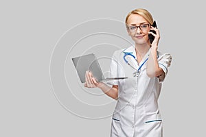Beautiful Caucasian woman doctor or nurse holding a laptop pc computer standing over grey background
