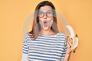 Beautiful caucasian woman eating banana as healthy snack scared and amazed with open mouth for surprise, disbelief face