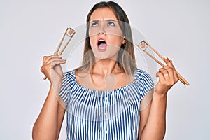 Beautiful caucasian woman eating sushi using chopsticks angry and mad screaming frustrated and furious, shouting with anger