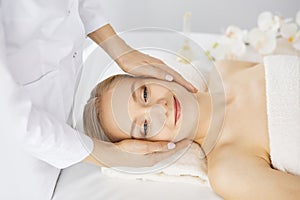 Beautiful caucasian woman enjoying facial massage with closed eyes in spa salon. Relaxing treatment in medicine and