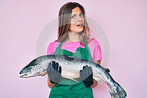 Beautiful caucasian woman fishmonger selling fresh raw salmon clueless and confused expression