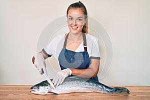 Beautiful caucasian woman fishmonger selling fresh raw salmon smiling with a happy and cool smile on face