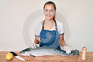 Beautiful caucasian woman fishmonger selling fresh raw salmon smiling with a happy and cool smile on face