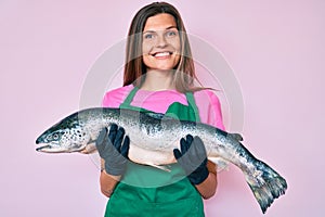 Beautiful caucasian woman fishmonger selling fresh raw salmon smiling with a happy and cool smile on face