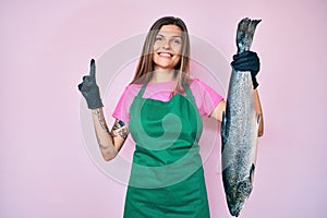 Beautiful caucasian woman fishmonger selling fresh raw salmon smiling with an idea or question pointing finger with happy face,