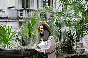 Beautiful caucasian woman in hat and casual beige clothes portrait on a background of palm leaves and ancient building