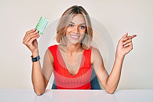 Beautiful caucasian woman holding birth control pills smiling happy pointing with hand and finger to the side