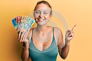 Beautiful caucasian woman holding canadian dollars smiling happy pointing with hand and finger to the side