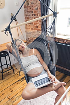 beautiful Caucasian woman holding a laptop and relaxing in the hammock