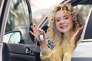 Beautiful Caucasian woman holds car keys sitting on the driver seat and smiling portrait copy space