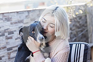 Beautiful caucasian woman hugging her dog pet sitting on chair at home terrace