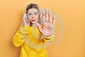 Beautiful caucasian woman listening to music using headphones with open hand doing stop sign with serious and confident