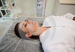 Beautiful Caucasian woman lying on a massage couch in a cosmetological clinic, relaxing during medical check-up, ready to receive