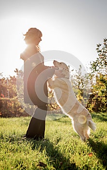 Beautiful caucasian woman playing with her golden labrador retriever dog at a park in the sunset