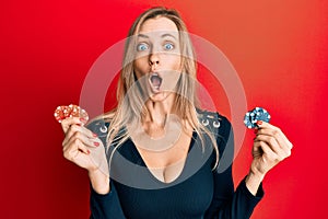 Beautiful caucasian woman playing poker holding casino chips afraid and shocked with surprise and amazed expression, fear and