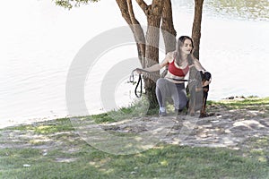 Beautiful caucasian woman posing with a cute doberman puppy on the lake