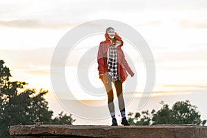 Beautiful Caucasian woman with red coat stand on the rock near the cliff on the mountain and background with warm light of sun