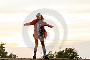 Beautiful Caucasian woman with red coat stand with spread her arms on the rock near the cliff on the mountain and background with