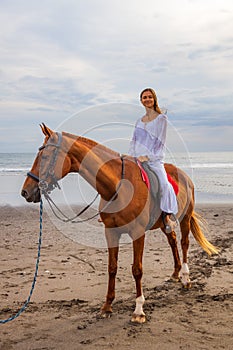 Beautiful caucasian woman riding horse on the beach. Female wearing white clothes. Copy space. Sunset time on the beach. Outdoor