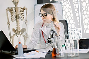 Beautiful Caucasian woman scientist in glasses preparing a microscope for laboratory testing and analysis, making notes