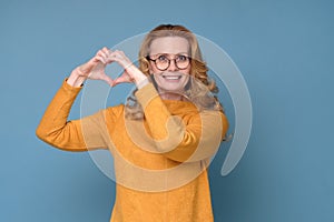 Beautiful caucasian woman showing heart shape isolated on blue background.