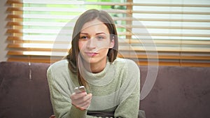 Beautiful caucasian woman sitting on couch with remote control watching television at home