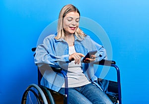 Beautiful caucasian woman sitting on wheelchair using smartphone looking positive and happy standing and smiling with a confident
