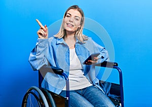 Beautiful caucasian woman sitting on wheelchair using smartphone smiling happy pointing with hand and finger to the side