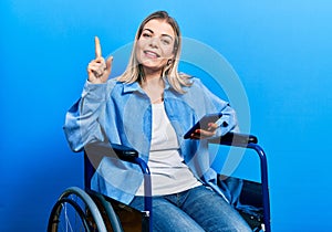 Beautiful caucasian woman sitting on wheelchair using smartphone smiling with an idea or question pointing finger with happy face,