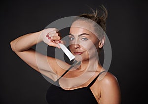 Beautiful Caucasian woman with tanned skin holding a tube of anti wrinkles smoothing anti puffiness under eyes cream, smiles