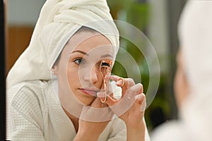 Beautiful caucasian woman using eyelash curler curling eyelashes before mascara in front of mirror