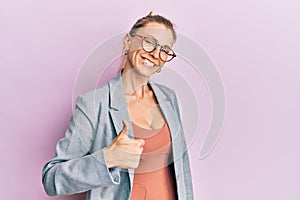 Beautiful caucasian woman wearing business jacket and glasses doing happy thumbs up gesture with hand