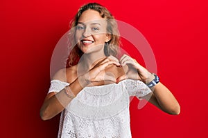 Beautiful caucasian woman wearing casual clothes over red background smiling in love showing heart symbol and shape with hands