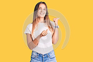 Beautiful caucasian woman wearing casual white tshirt pointing to the back behind with hand and thumbs up, smiling confident