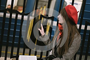 Beautiful Caucasian woman wearing coat, beret and scarf sitting alone on Saint Petersburg metro station with a book.