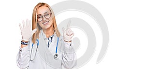 Beautiful caucasian woman wearing doctor uniform and stethoscope showing and pointing up with fingers number seven while smiling