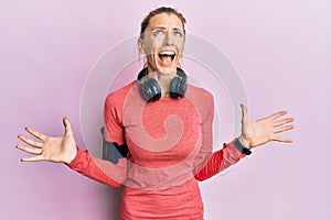 Beautiful caucasian woman wearing sportswear and arm band crazy and mad shouting and yelling with aggressive expression and arms