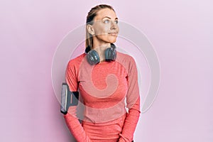 Beautiful caucasian woman wearing sportswear and arm band looking away to side with smile on face, natural expression