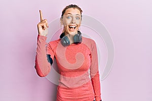 Beautiful caucasian woman wearing sportswear and arm band pointing finger up with successful idea