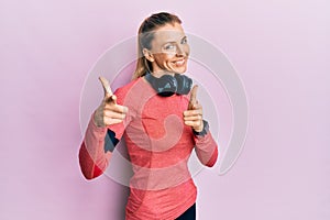 Beautiful caucasian woman wearing sportswear and arm band pointing fingers to camera with happy and funny face
