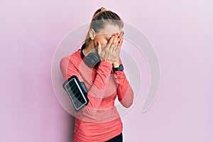 Beautiful caucasian woman wearing sportswear and arm band with sad expression covering face with hands while crying