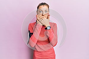 Beautiful caucasian woman wearing sportswear and arm band shocked covering mouth with hands for mistake