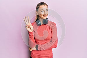 Beautiful caucasian woman wearing sportswear and arm band showing and pointing up with fingers number three while smiling