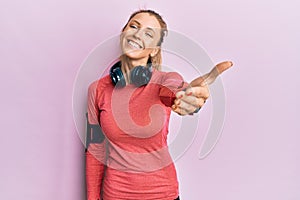 Beautiful caucasian woman wearing sportswear and arm band smiling friendly offering handshake as greeting and welcoming