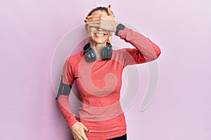 Beautiful caucasian woman wearing sportswear and arm band smiling and laughing with hand on face covering eyes for surprise