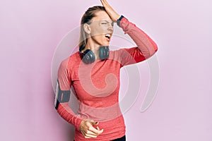 Beautiful caucasian woman wearing sportswear and arm band surprised with hand on head for mistake, remember error