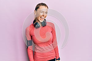 Beautiful caucasian woman wearing sportswear and arm band winking looking at the camera with sexy expression, cheerful and happy
