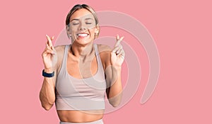 Beautiful caucasian woman wearing sportswear gesturing finger crossed smiling with hope and eyes closed