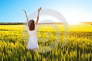 Beautiful caucasian woman in white dress jumping up with raised hands outdoor. Field with yellow wheat around